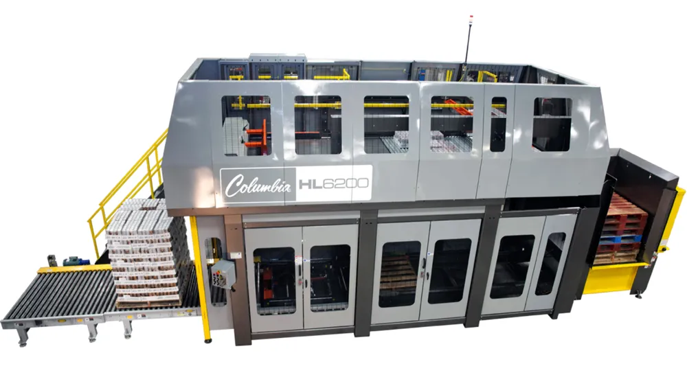 A large enclosed high-level palletizer with windows, an operator stair on the left, and a roller conveyor at the infeed.